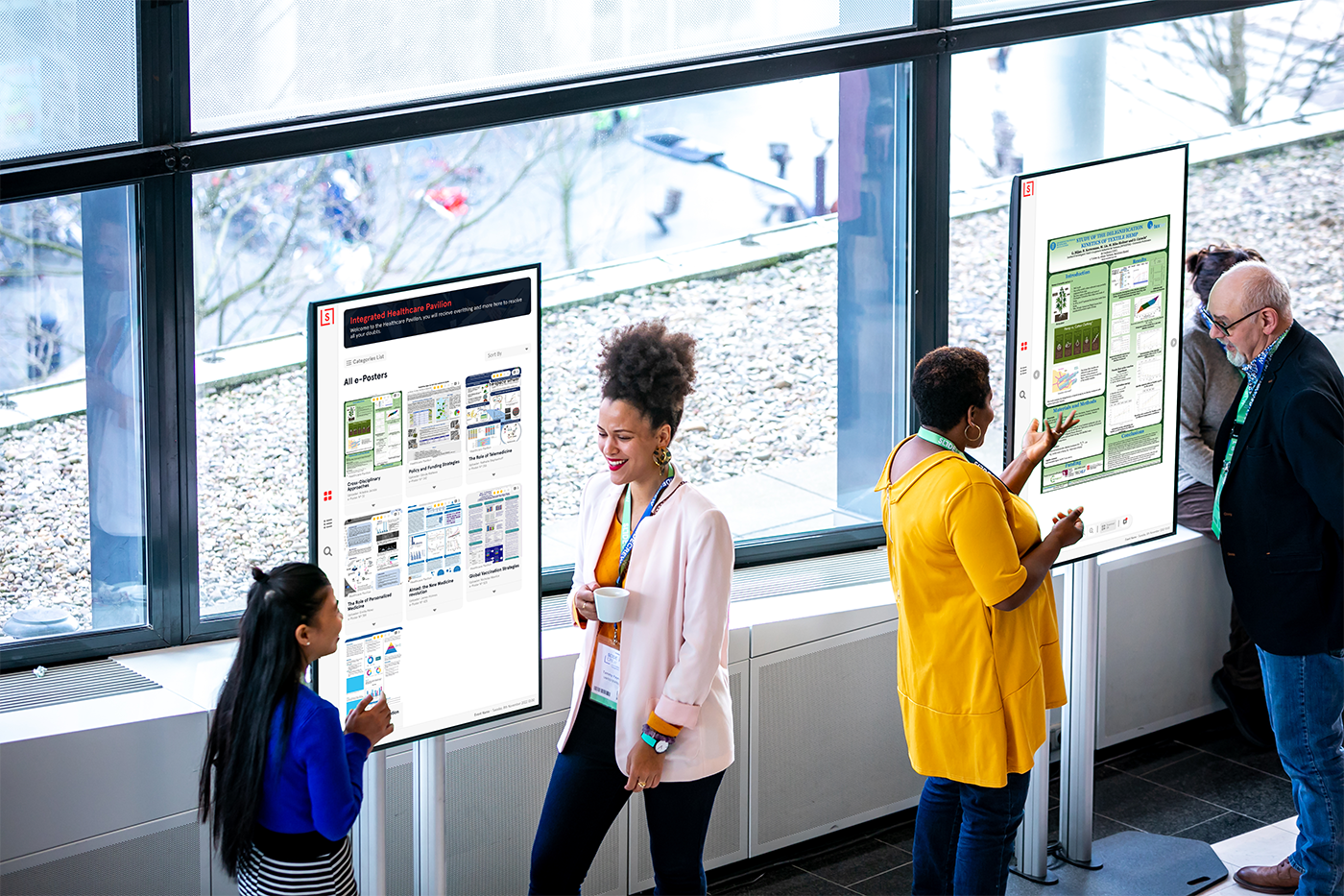 ePoster multitouch screens in front of a window and people talking and discussing the posters.