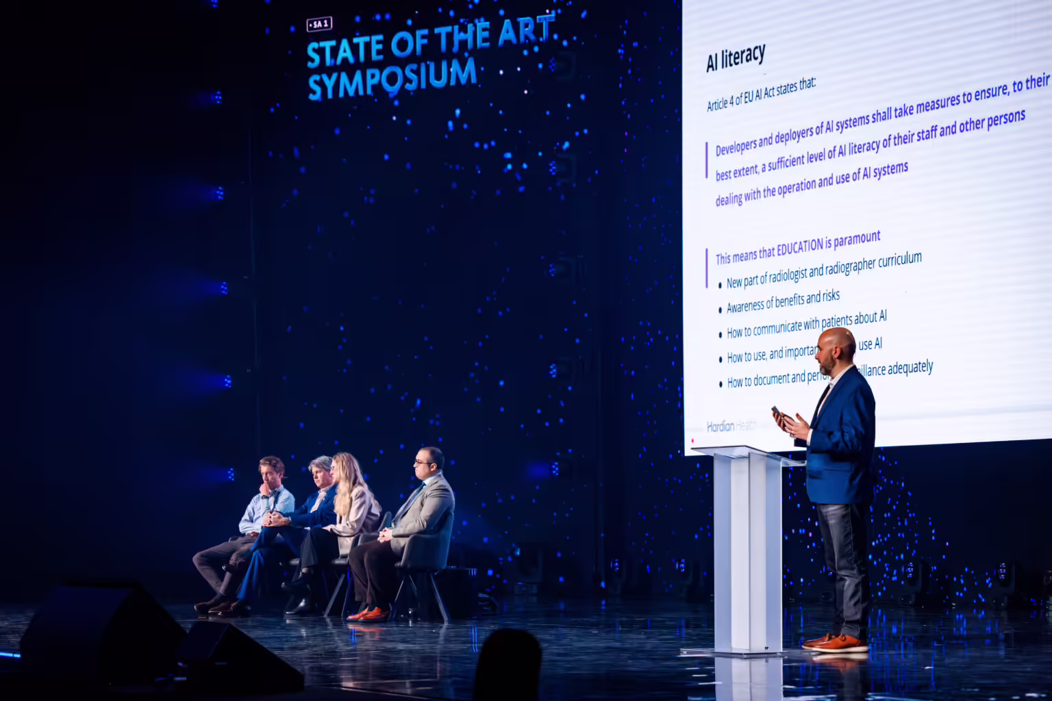 Conference speaker delivering a lecture in a large event hall after successfully reviewing and preparing their presentation in the Slidecrew Speaker Ready Room.