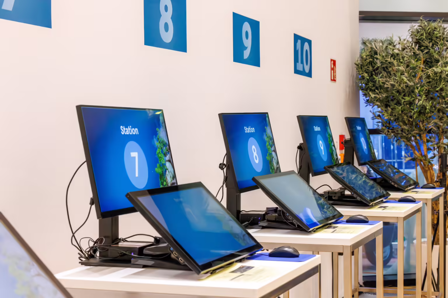 Self-service speaker preview station setup with multiple standing desks in a row, featuring Slidecrew’s speaker-ready system for fast and independent presentation checks at conferences.